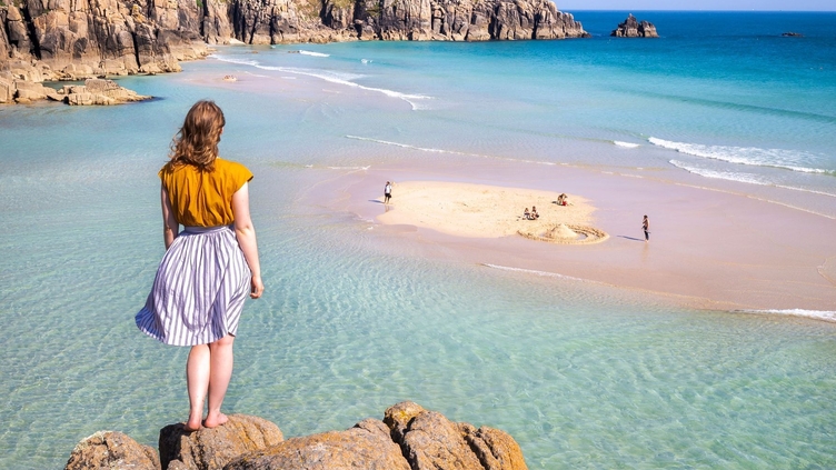 Woman, stood atop a stack of rocks, looking out to sea